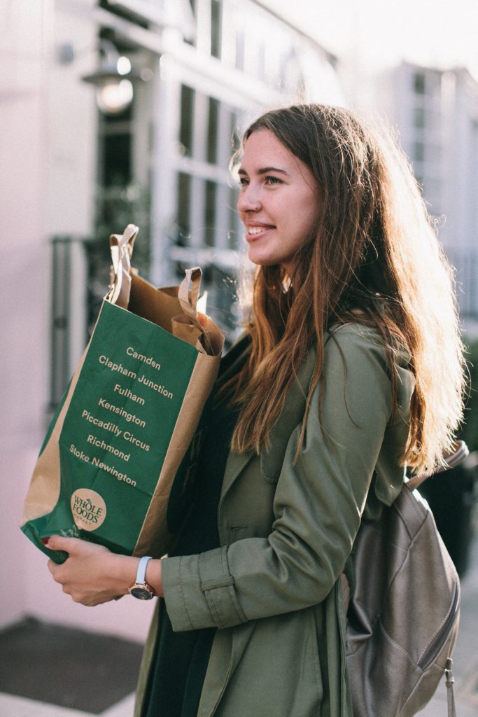 Girl in a green jacket holding a paper Whole Foods bag