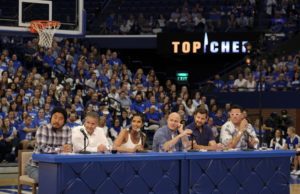 rupp arena: group of people sitting at a table with a big crowd behind them