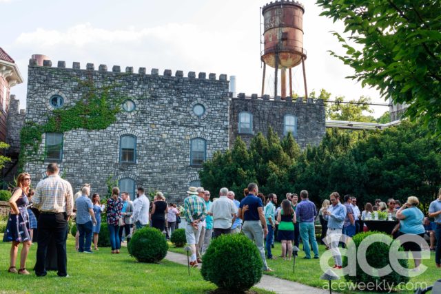 Castle & Key: outside shot of people in a garden and a tall water tower and stone building behind them