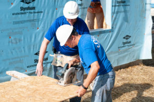 two men wearing blue shirts and white hard hats building