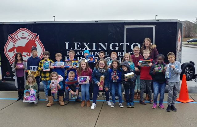 Toy Drive: kids holding toys standing in front of a trailer that says Lexington Fraternal order of Firefighters