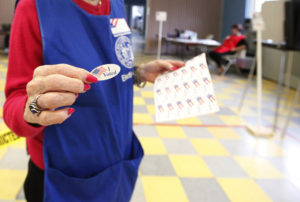 Community: Volunteer handing out I Voted stickers after filling out a election ballot at a district voting station
